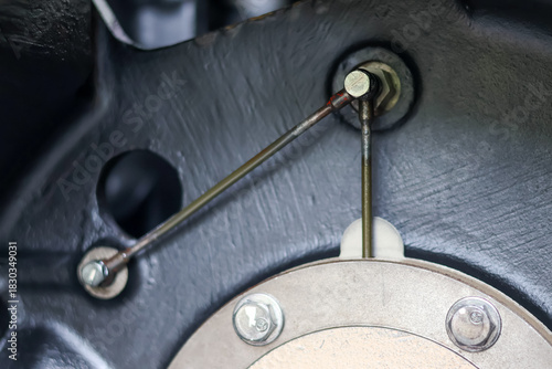 Detail shot of a metal linkage and lubrication line connection point, bolted onto a circular flange and dark, textured industrial casting, emphasizing precision and maintenance.