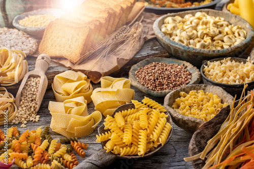 Different types of uncooked pasta on rustic wooden table, in the spoons, cutting board and bowls 