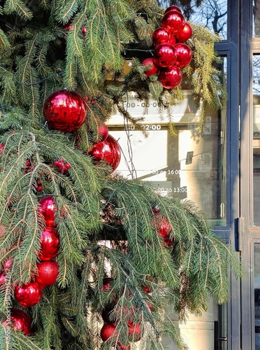 Close-up of Christmas decorations made of fir branches and shiny red ornaments with reflections. Festive holiday composition featuring traditional winter decor and bright seasonal colors.
