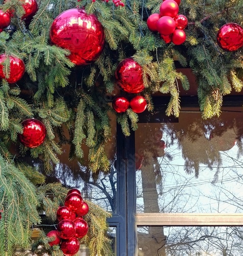 Close-up of Christmas decorations made of fir branches and shiny red ornaments with reflections. Festive holiday composition featuring traditional winter decor and bright seasonal colors.