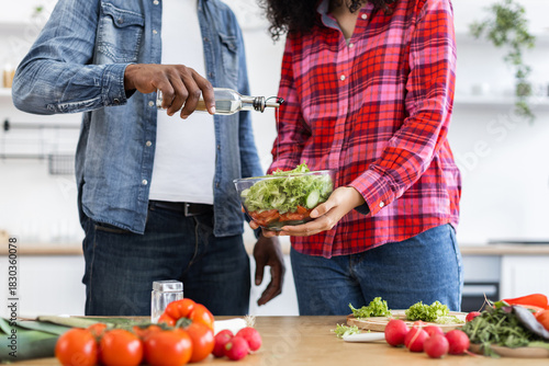 A couple prepares a healthy salad together in a bright kitchen, adding dressing to the fresh ingredients.