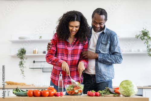 An African-American couple prepares a healthy salad together in a bright, modern kitchen, embracing a lifestyle of wellness and togetherness.