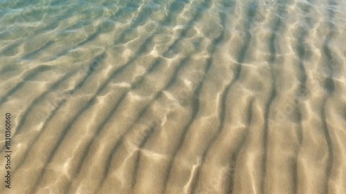 Sunlight filtering through clear water creating beautiful ripple patterns on the sandy seabed.