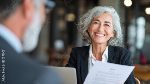 Fototapeta Naklejka Na Ścianę i Meble -  Smiling mature business woman hr holding cv document at job interview. Happy mid aged professional banking manager or lawyer consulting client sitting at workplace in corporate office meeting.