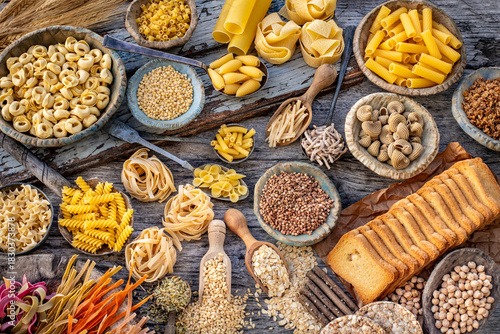 Different types of uncooked pasta on rustic wooden table, in the spoons, cutting board and bowls 