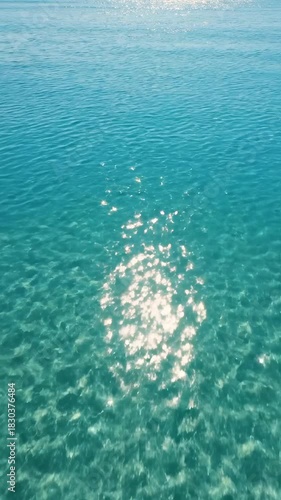 Drone aerial view sweeping over calm shallow ocean water with dazzling sun glimmers moving across the vibrant blue surface texture dazzling sun glimmers, high angle, texture