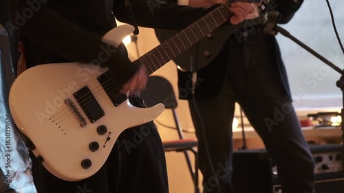 Guitarist in dark clothing plays white electric guitar on stage capturing energy and focus during live music performance