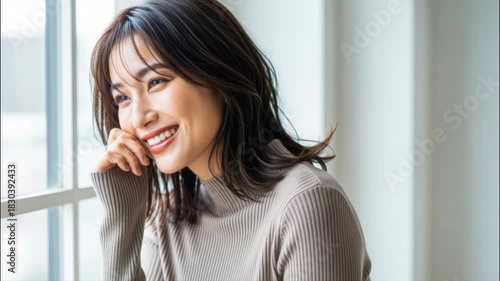 窓辺で楽しそうに微笑むニットワンピースの女性