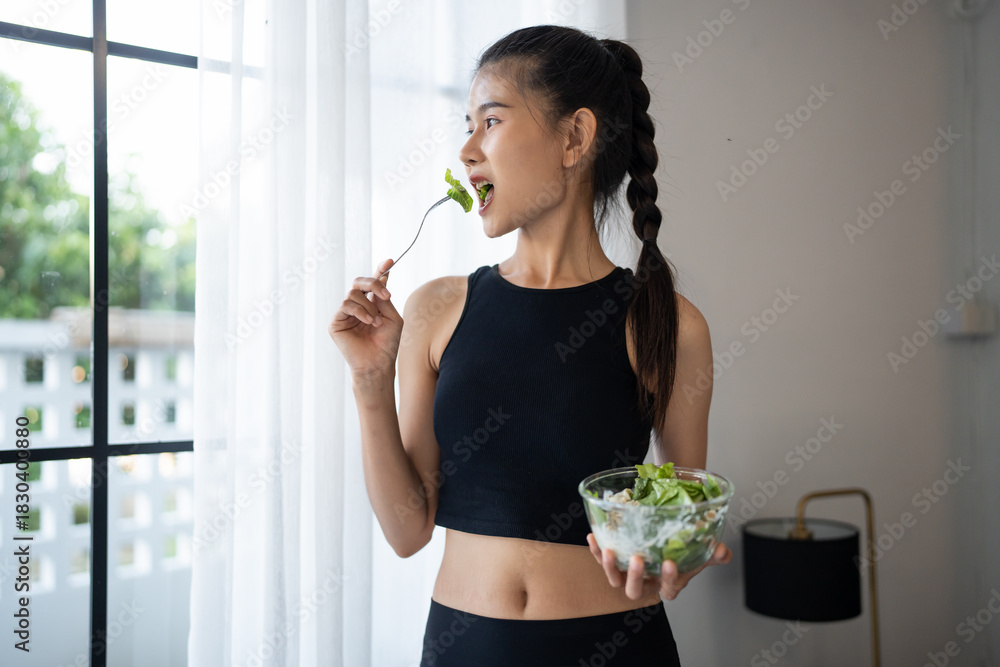 Naklejka premium Fitness asian woman eating healthy salad after workout. Smiling Beautiful asian young female eating healthy food after exercise training in yoga studio healthy lifestyle