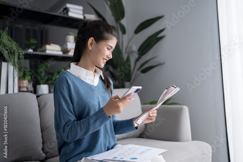 Asian woman holding paper document calculating money savings paying bills in mobile application using smart phone payment online with paying household bills tax insurance managing budget