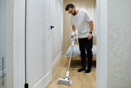 Man using a vacuum cleaner while cleaning a wooden floor in a modern home interior during day time