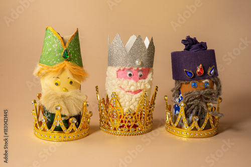 Fotografie Three handmade Three Kings figurines placed inside of crowns are displayed on a beige background, symbolizing Epiphany celebration on January 6