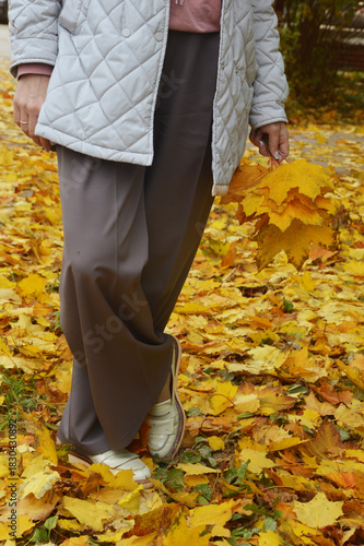 Women's legs in brown trousers against the background of yellow autumn leaves.