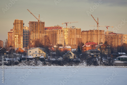 Construction of a city multi-story building on the river bank in winter in sunset colors