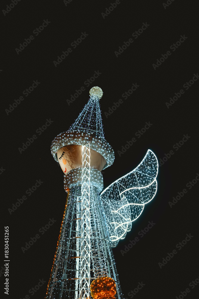 Obraz premium Giant glowing angel figure with wings at night, illuminated by white and blue lights.