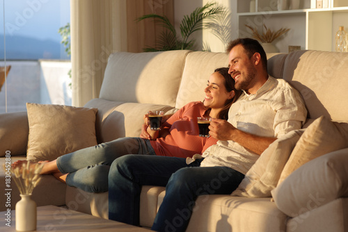 Happy couple in love drinking coffee at home looking away