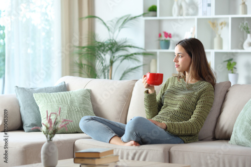 Relaxed woman in green drinking coffee from red mug looking away