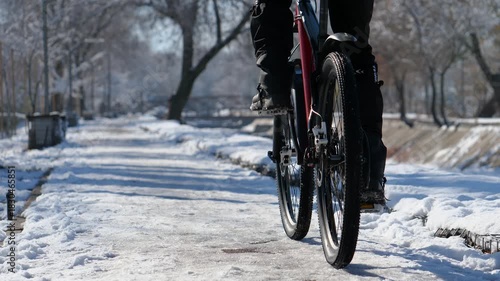 A cyclist rides along an icy sidewalk on a winter day. Close-up. Active lifestyle in winter.