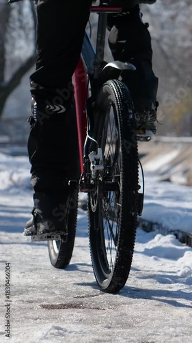 Vertical video footage of a cyclist rides along an icy sidewalk on a winter day. Close-up. Active lifestyle in winter.
