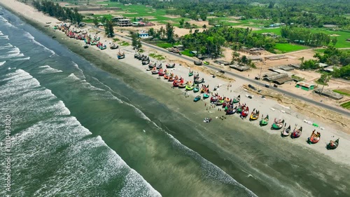Aerial view of colorful fishing boats lined up on a sandy beach next to the ocean waves Teknaf, Cox's Bazar, Bangladesh