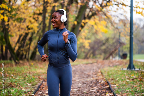 A runner in dark athletic wear moves confidently down a wooded path, framed by vibrant fall foliage and soft natural light.