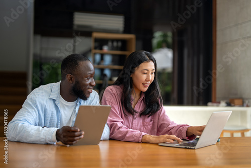 Business team, two happy diverse, multiethnic executives working together using laptop in office.
