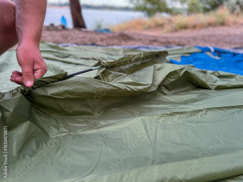 Person setting up camping tent on sandy beach