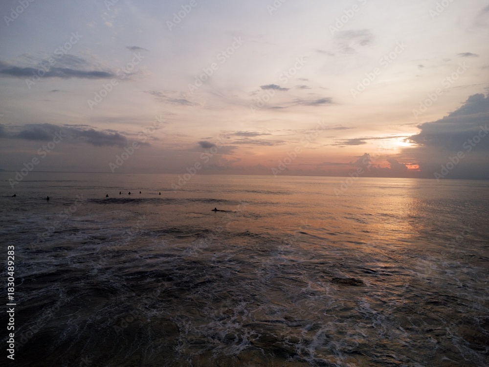 Naklejka premium Surfers waiting at sunrise with glowing horizon