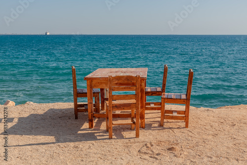 Fototapeta Naklejka Na Ścianę i Meble -  Wooden table and chairs on a beach by the Mediterranean Sea.