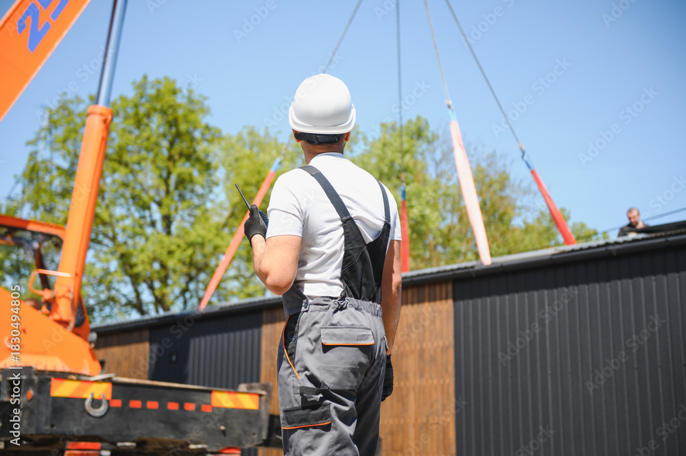 Naklejka premium Construction worker supervising lifting of modular house onto truck