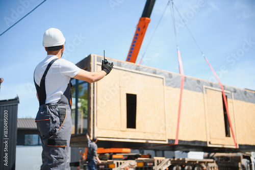 Obraz na plátne Construction worker directing crane lifting prefabricated house onto truck