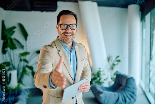 Bild auf Leinwand Smiling businessman holding a tablet, extending hand forward, offering a greetin