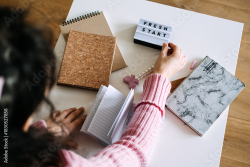 Person sits at white table touching FRESH START light box next to small open notebook and planner covers. Creative journaling, New Year goals, visual goal setting, productivity planning.