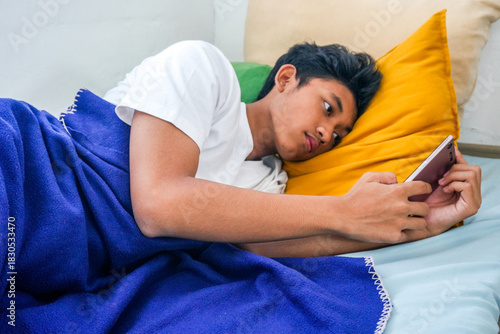 Teenager Relaxing In Bed With Smartphone While Scrolling Social Media With Blanket And Pillows