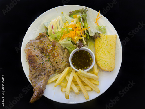 Pork steak served with fries, salad, garlic bread and a sauce in the middle.