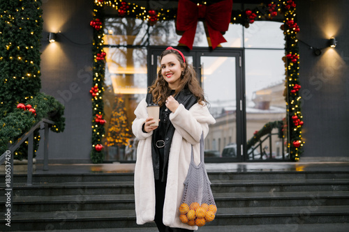 Young caucasian female holding oranges and coffee in festive urban setting