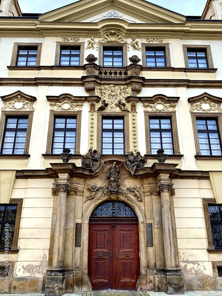 Fototapeta premium Baroque-style building in Hradec Kralove, Czech Republic. Features an elaborate facade with intricate stucco decorations, pilasters, and ornamental sculptures above the entrance.