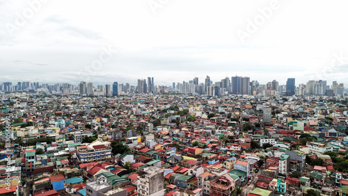 High angle drone view of the San Andres district in Manila, Philippines, showing a dense maze of colorful low-rise houses in the foreground. The modern skyscrapers of Makati City’s central business.