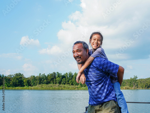 Happy Father Giving Daughter Piggyback Ride Near Lake in Summer.