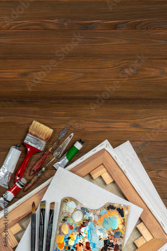 Old used brushes and palette knife in an artist's studio, palette with multi-colored spots of oil or acrylic paint, paint tubes, stretched canvases. Copy space