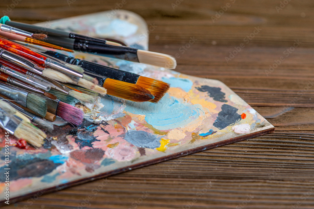 Obraz premium Old used brushes in an artist's studio, palette with multi-colored spots of oil or acrylic paint