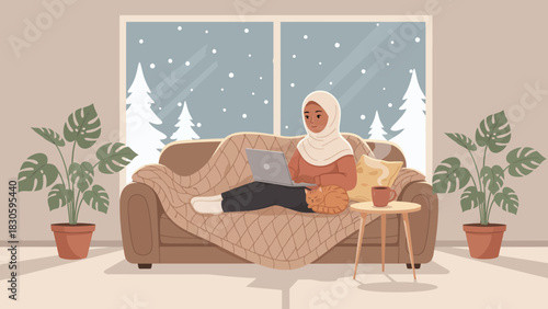 A woman in a hijab sitting on a cozy sofa with a blanket, using a laptop, while snow falls outside the window.