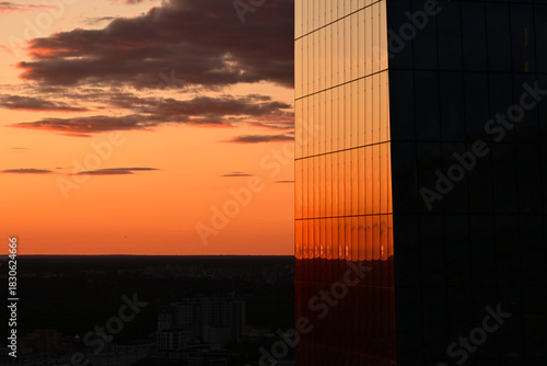 The orange sky reflecting in the glass panes of a skyscraper. Scenic sunset in a big city concept. Warsaw, Poland