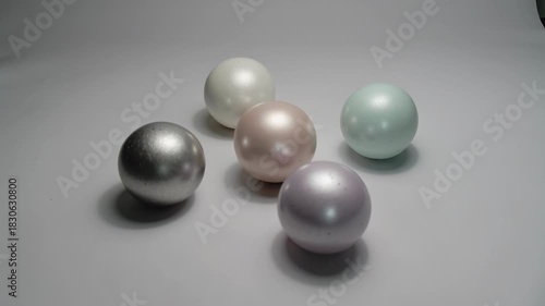 Elegant arrangement of five pastel-colored spheres on a smooth gray surface, featuring soft lighting and subtle shadows, highlighting the delicate hues of silver, lavender, mint, cream, and blush pink