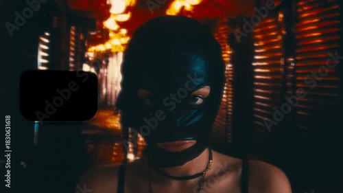 Woman in a black latex balaclava raises her eyes to the camera. Heavy 16mm film grain, noise, and sprocket hole overlay create a grunge underground aesthetic with a shaky street background.