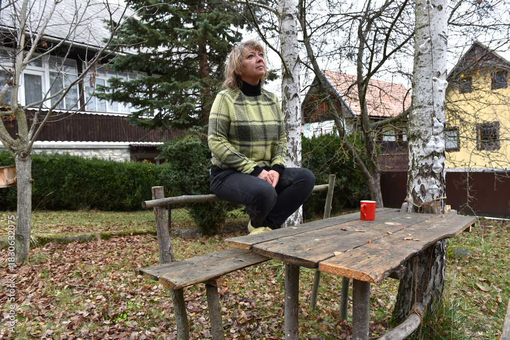 Fototapeta premium Woman sitting on a rustic wooden bench looking up at the trees