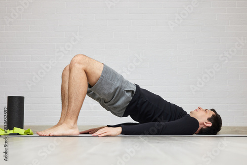 Man doing glute bridge on a mat indoors for fitness and strength training