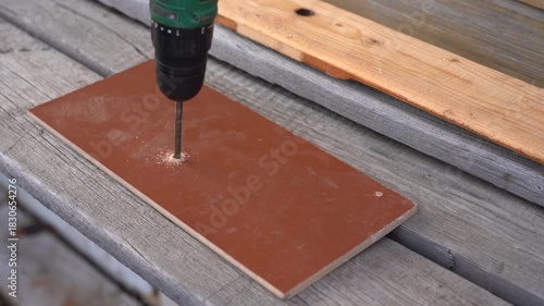 Precision Drilling in Action: A Close-Up of a Drill Penetrating a Brown Tile on a Wooden Surface, Showcasing Craftsmanship and Tool Usage. Video with sound