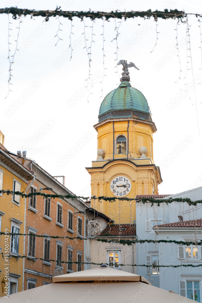 Naklejka premium The iconic City Clock Tower (Gradski Toranj) in Rijeka, Croatia, framed by festive Christmas lights hanging across the street