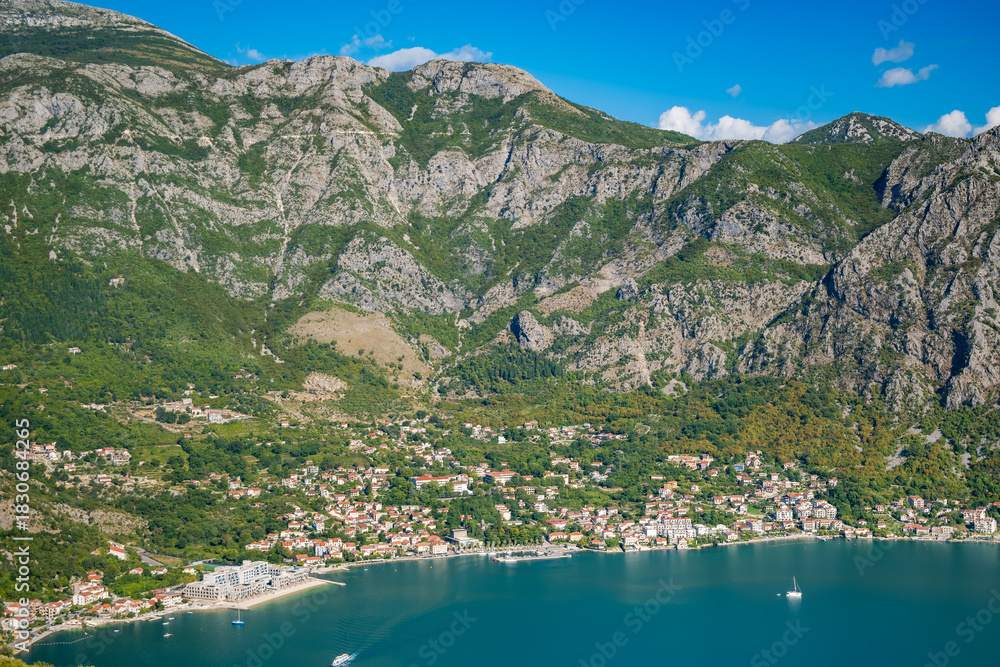 Naklejka premium Aerial view of a coastal town Risan in Montenegro, surrounded by mountains and clear blue water. Lush greenery and small boats are visible in the bay.